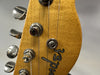 Close-up of Fender guitar headstock with tuning pegs and strings on natural wood finish.