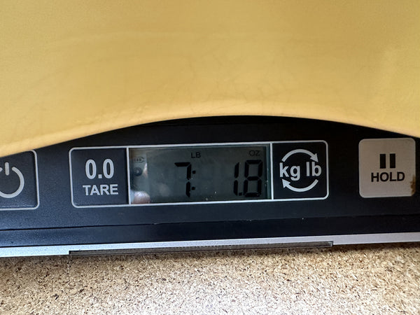 Digital scale showing guitar weight of 7 pounds 1.8 ounces on cork surface background