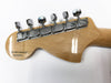 Close-up of maple guitar headstock with six chrome tuning pegs and serial number MX11084383, made in Mexico, on a white background