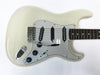 White electric guitar with rosewood fretboard, three single-coil pickups, whammy bar, and black tone and volume knobs on a white background