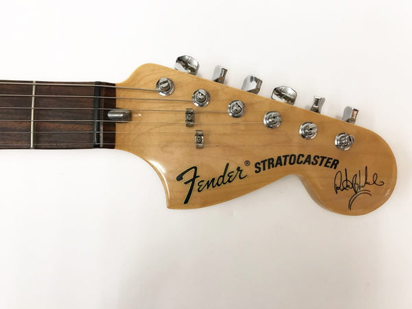 Close-up of Fender Stratocaster guitar headstock with six chrome tuning pegs and signature on natural wood finish