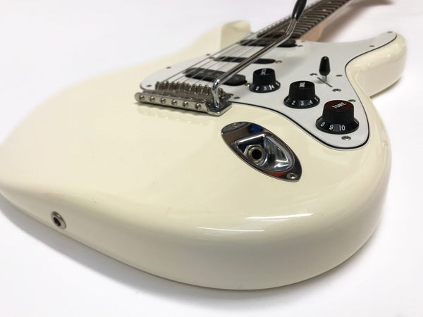 Close-up of white electric guitar body with chrome bridge, black tone and volume knobs, white pickguard, and input jack on white background