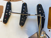 Close-up image of vintage single coil guitar pickups mounted on a white pickguard, showing cloth-covered wires and handwritten markings on the black pickup covers.
