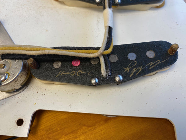Close-up of vintage Fender Stratocaster guitar single coil pickup with cloth-covered wires and dated signature on black bobbin mounting plate