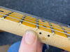 Close-up of electric guitar maple neck and fretboard showing metal frets and wound strings with finger on side dot markers