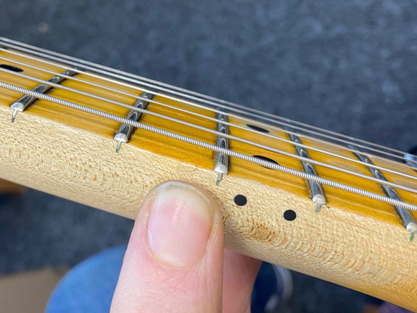 Close-up of electric guitar maple neck and fretboard showing metal frets and wound strings with finger on side dot markers