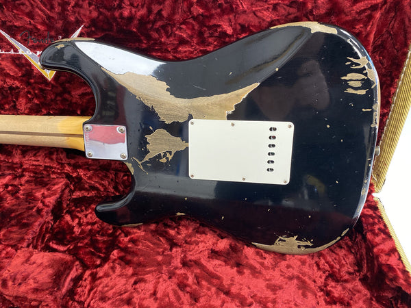 Worn black electric guitar body with visible wood patches and white backplate, resting in red velvet-lined guitar case