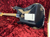 Vintage black electric guitar with worn and chipped paint finish, showing wood underneath, resting on red velvet fabric inside guitar case