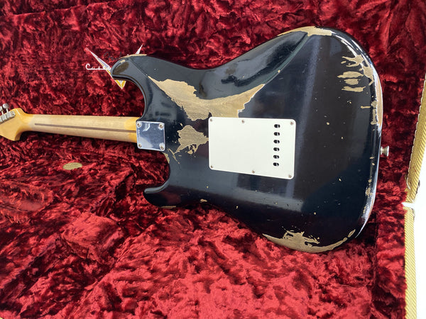 Vintage black electric guitar with worn and chipped paint finish, showing wood underneath, resting on red velvet fabric inside guitar case