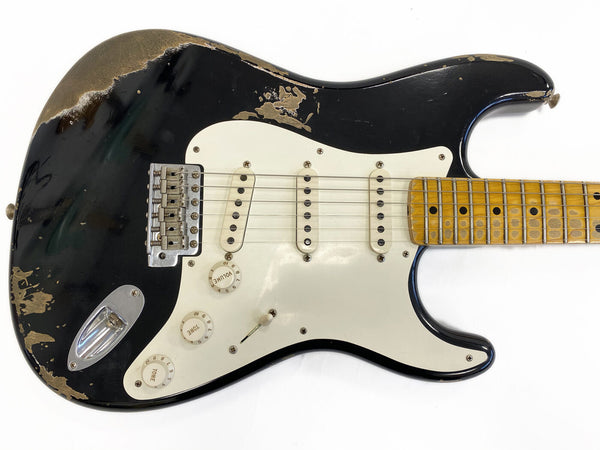 Vintage black electric guitar with worn finish, three single-coil pickups, white pickguard, and maple neck with dot inlays on fingerboard against white background
