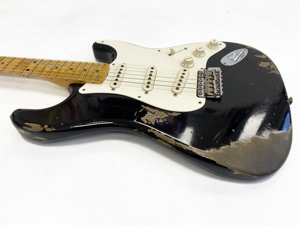 Black electric guitar with white pickguard and maple neck showing heavy wear and paint chipping on body, three single-coil pickups, and vintage-style tremolo bridge on white background
