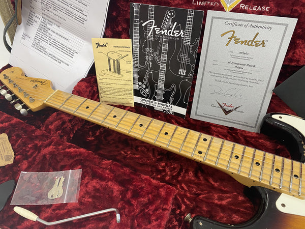 Fender Stratocaster Relic electric guitar neck and headstock close-up with owner's manual, tremolo springs diagram, certificate of authenticity, and guitar case interior with red plush lining and accessories.