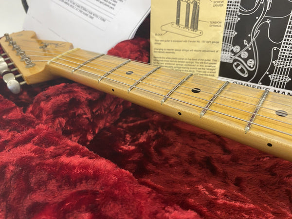Close-up of electric guitar maple neck and strings in red plush guitar case with instruction manuals in background