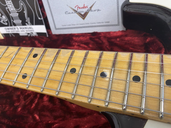 Close-up of Fender guitar maple neck and fretboard with black dot inlays and strings, inside plush red guitar case with Fender Custom Shop paperwork in background.