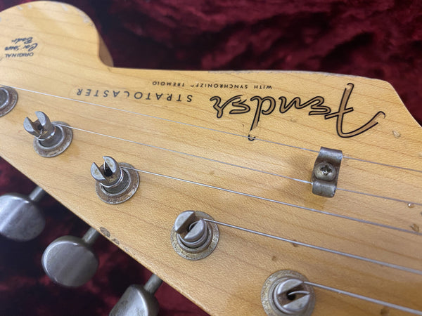 Close-up of Fender Stratocaster guitar headstock with vintage tuning pegs and SynchroLock tremolo system, natural wood finish on red velvet background.
