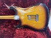 Back side of vintage sunburst Fender Stratocaster guitar showing worn finish, tremolo springs, and maple neck, displayed in red velvet Fender Custom Limited guitar case