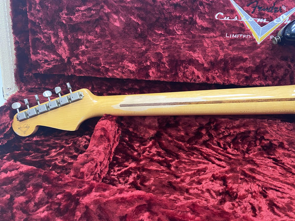 Back of Fender Custom Shop electric guitar neck with vintage tuners resting in plush red velvet guitar case interior