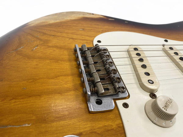 Close-up view of vintage Fender-style guitar bridge, white pickguard, and volume knob on sunburst electric guitar body with worn wood finish