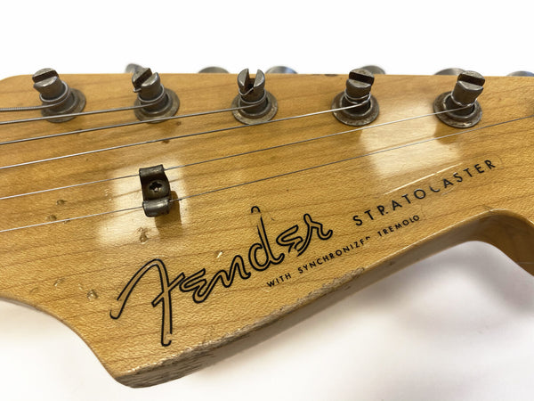 Close-up of vintage Fender Stratocaster guitar headstock with tuning pegs and strings, showing wear and "with synchronized tremolo" text