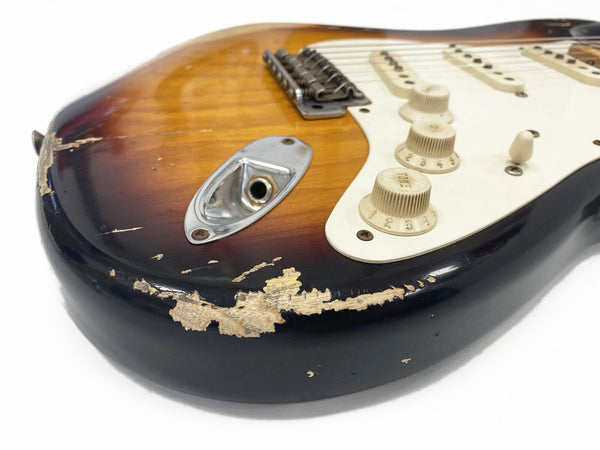 Close-up of vintage sunburst electric guitar body with worn and chipped finish, showing input jack and white control knobs on cream pickguard