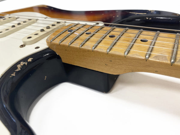 Close-up of maple neck and fretboard with dot inlays on worn sunburst electric guitar body featuring white single-coil pickups and black pickguard.