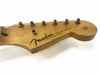 Fender Stratocaster guitar headstock with six tuning pegs, natural wood finish, worn edges, and vintage logo on white background