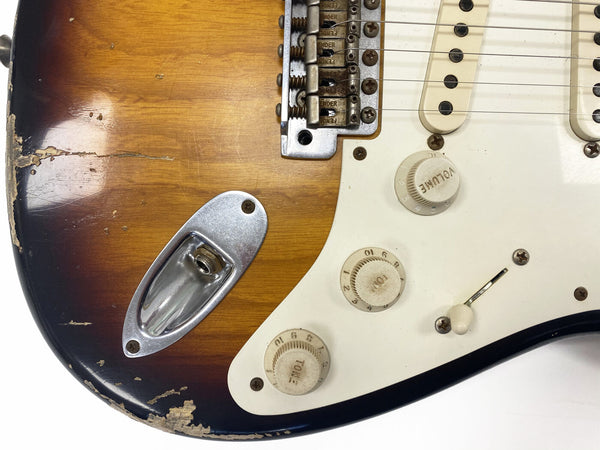 Close-up of worn vintage sunburst Fender Stratocaster electric guitar body showing volume and tone control knobs, pickup covers, input jack, and chipped finish.