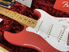 Close-up of red Fender Stratocaster electric guitar with maple neck and white pickguard in plush red guitar case, showing pickups, volume knob, and part of the headstock area with documents and Fender logo visible.