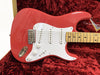 Red Fender Stratocaster electric guitar with white pickguard and maple neck resting in plush red case interior