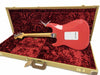 Back of coral red Fender electric guitar with maple neck resting inside an open vintage-style tweed case lined with plush red velvet
