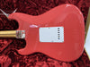Back of coral pink Fender electric guitar body with white backplate, maple neck, and chrome neck plate on red plush guitar case lining