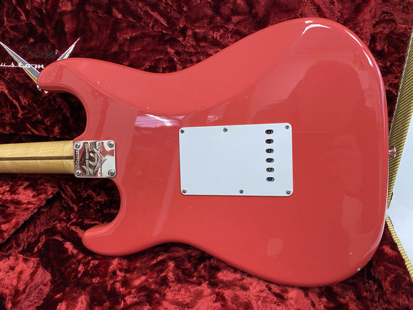 Back of coral pink Fender electric guitar body with white backplate, maple neck, and chrome neck plate on red plush guitar case lining