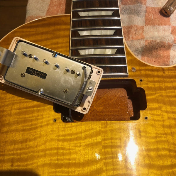 Close-up of guitar pickup cavity with removed humbucker pickup on amber flame maple guitar top and rosewood fretboard with trapezoid inlays.