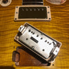 Close-up of guitar humbucker pickup removed from electric guitar body showing metal cover with "Patent Applied For" label on amber flame maple top.