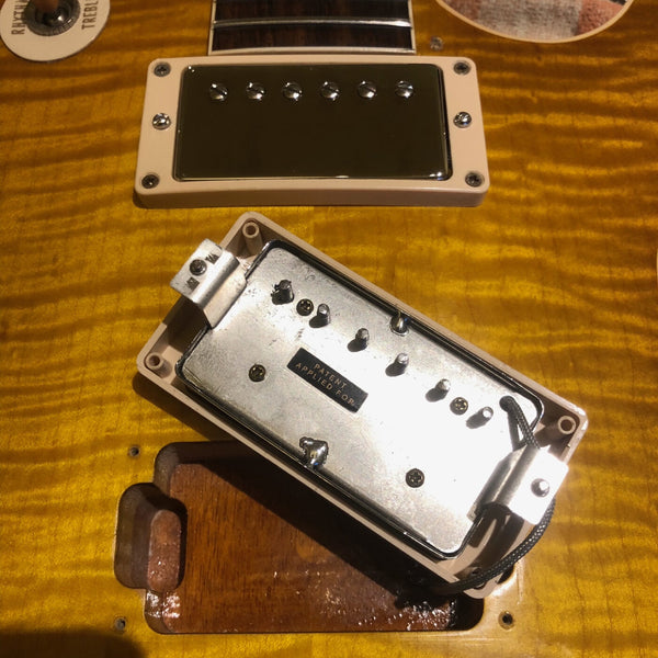 Close-up of guitar humbucker pickup removed from electric guitar body showing metal cover with "Patent Applied For" label on amber flame maple top.