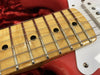 Close-up of maple fretboard with metal frets and black dot inlays on red electric guitar body with white pickguard and chrome screw, detailed guitar neck and strings view