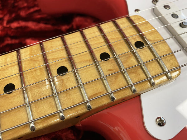 Close-up of maple fretboard with metal frets and black dot inlays on red electric guitar body with white pickguard and chrome screw, detailed guitar neck and strings view