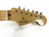Close-up of Fender Stratocaster guitar headstock with six tuning pegs and "Fender Stratocaster with Synchronized Tremolo" logo on natural wood finish