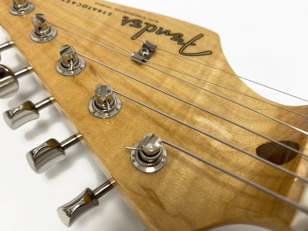 Close-up of Fender Stratocaster electric guitar maple headstock with chrome tuning pegs and strings against white background