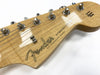 Close-up of natural wood Fender Stratocaster guitar headstock with tuning pegs and strings, featuring original contour body label and synchronized tremolo text