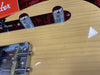 Close-up of Fender electric guitar control knobs and bridge on light wood finish guitar body with red Fender tag in background