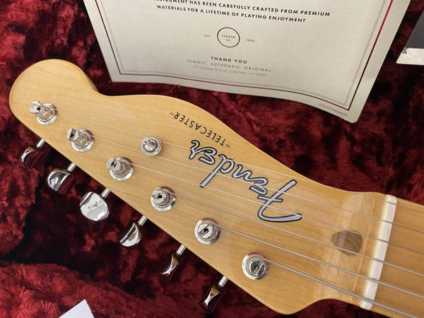 Close-up of Fender Telecaster guitar headstock with tuning pegs and strings on red plush case interior, certificate of authenticity in background