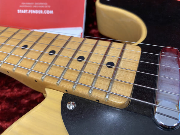 Close-up of maple guitar neck with black dot inlays, steel strings, and black pickguard on electric guitar body in case
