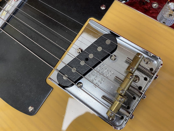 Close-up of Fender Telecaster bridge and pickup with vintage-style brass saddles and Fender patent number engraved on the metal plate, showcasing honey blonde guitar body and black pickguard.
