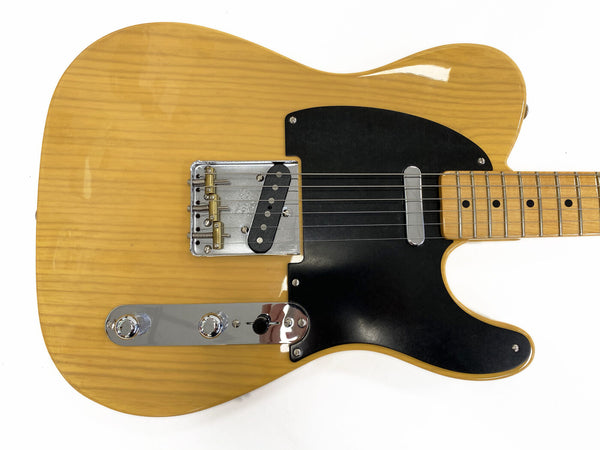 Electric guitar with natural wood finish, black pickguard, chrome bridge, control knobs, and maple fretboard with dot inlays on white background