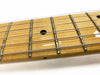 Close-up image of maple guitar neck with metal frets and black dot inlays on fretboard, steel guitar strings visible