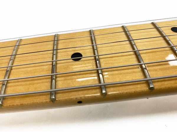 Close-up image of maple guitar neck with metal frets and black dot inlays on fretboard, steel guitar strings visible
