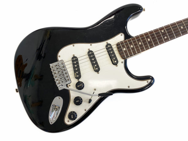 Black electric guitar with white pickguard and three EMG single-coil pickups, volume and tone control knobs, and tremolo bridge system on white background