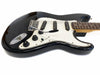 Black electric guitar with white pickguard and three single-coil pickups, close-up view of body and neck on white background