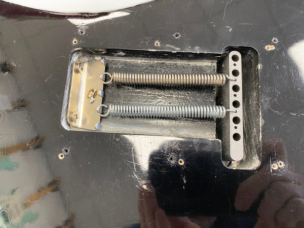 Close-up of electric guitar tremolo cavity showing two metal springs and claw on a worn black guitar body
